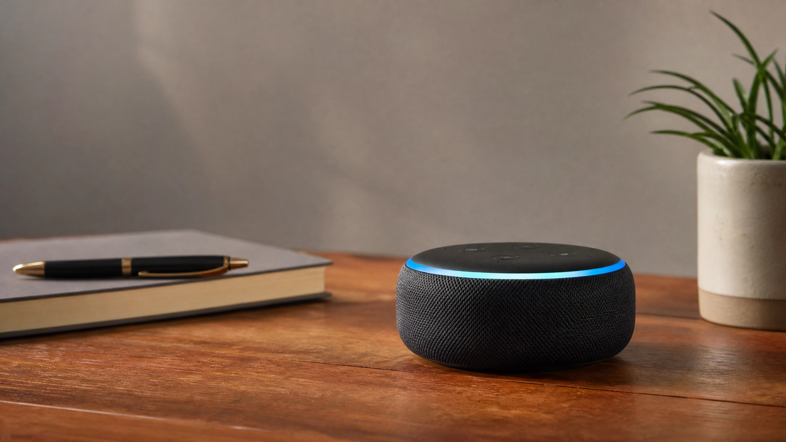 Echo Dot preto com anel azul sobre mesa de madeira ao lado de caderno e planta